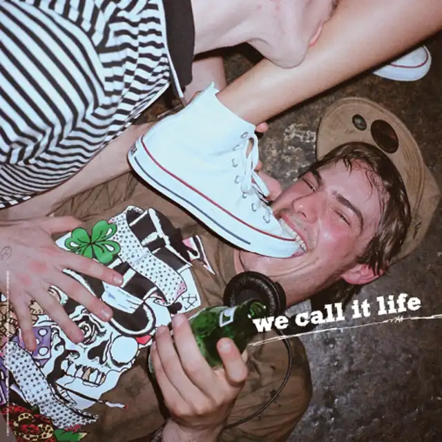 Partybesucher, der fröhlich auf dem Boden liegt und in einen Converse Schuh beißt